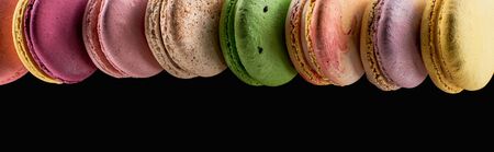 row of tasty colorful French macaroons of different flavors isolated on black with copy space,...