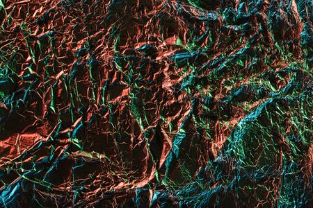 top view of glossy crumpled foil with colorful lighting reflection in darknessの写真素材