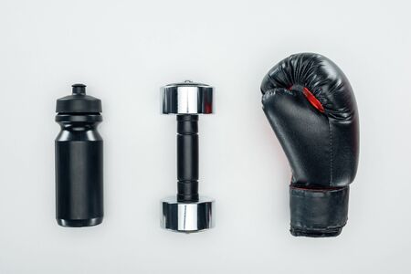 top view of black sport bottle near dumbbell and boxing glove isolated on white