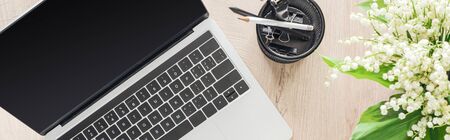 panoramic view of laptop, stationery and flowers on wooden tableの写真素材