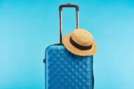 blue colorful travel bag with handle and straw hat isolated on blueの写真素材