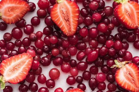 top view of red, fresh and ripe cranberries, cut strawberriesの写真素材