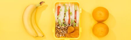 panoramic shot of lunch box with food near bananas and oranges