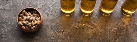 panoramic shot of bottles of light beer near pistachios on brown textured surfaceの写真素材