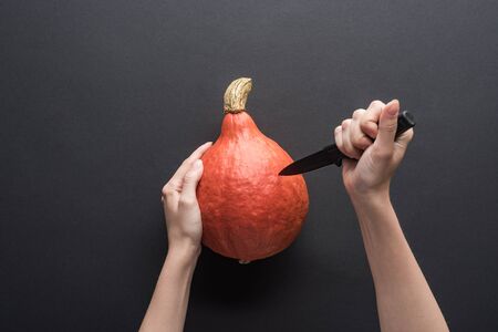 cropped view of woman carving Halloween pumpkin on black background