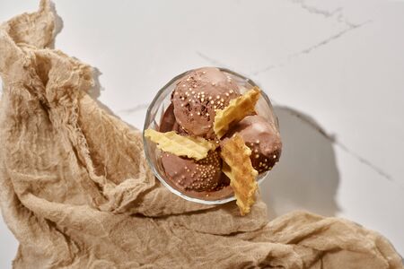 top view of delicious chocolate ice cream in bowl with waffles near brown cloth on marble grey...