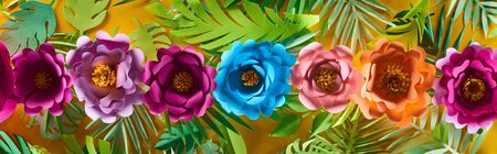 flat lay with paper cut flowers on tropical leaves on yellow bright background, panoramic shot