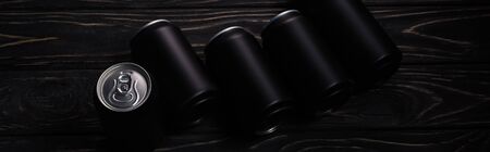 panoramic shot of black metallic cans of beer on wooden tableの写真素材