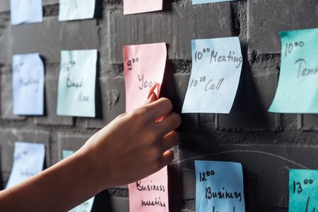 cropped view of woman attach pink colorful sticker note on black brick wall