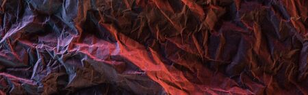 top view of glossy crumpled foil with colorful lighting reflection in darkness isolated on black