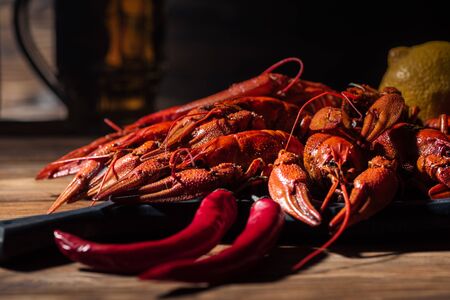 selective focus of red lobsters, tomatoes, lemon, peppers and glass with beer on wooden surfaceの写真素材