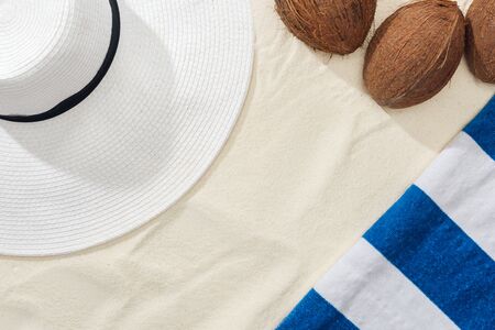 top view of coconuts, striped towel and white straw hat on sandの写真素材