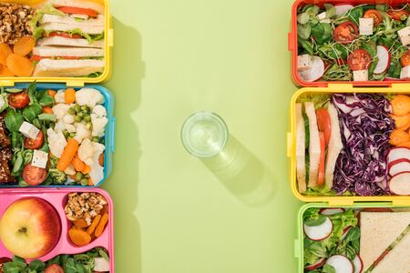 top view of lunch boxes with food near glass of waterの写真素材