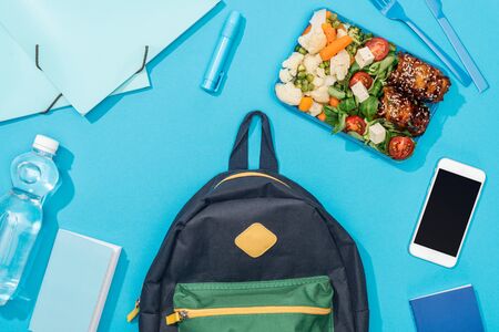 top view of backpack near lunch box, stationery, smartphone and bottle of waterの写真素材