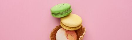 top view of multicolored delicious French macaroons in crispy waffle cone on pink background,...