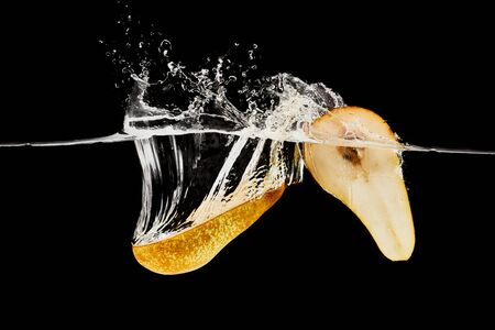 pear halves falling in water with splash isolated on blackの写真素材