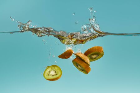kiwi slices falling deep in water with splash on blue backgroundの写真素材