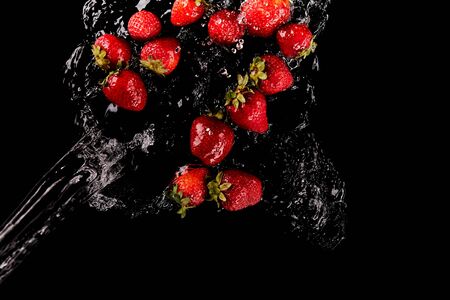 top view of ripe red strawberries with water splash isolated on blackの写真素材