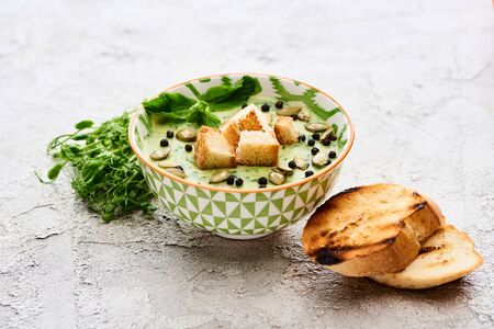 bowl of delicious green vegetable creamy soup with croutons, sprouts, black pepper and pumpkin seeds