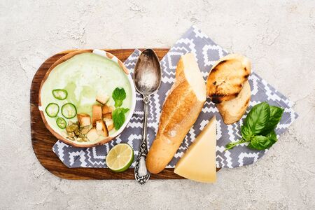 top view of green vegetable creamy soup on wooden chopping board with napkin, spoon and ingredientsの写真素材