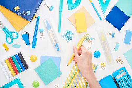 Cropped image of schoolgirl holding yellow pen near stationery isolated on white