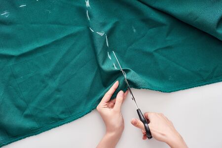 top view of seamstress cutting colorful fabric with scissors on white background