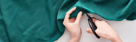 panoramic shot of seamstress cutting colorful fabric with scissors on white background
