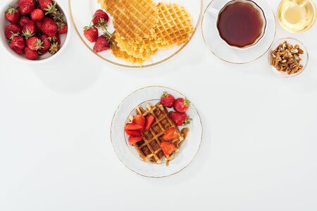 top view of delicious breakfast with waffles, strawberries and tea on whiteの写真素材
