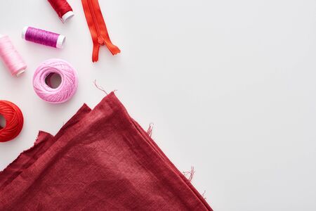 top view of colorful threads, knitting yarn balls, fabric and zippers on white background