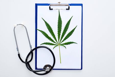 top view of medical cannabis leaf on clipboard near stethoscope on white backgroundの写真素材