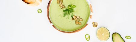 panoramic shot of delicious creamy green vegetable soup near lime and jalapenos isolated on white