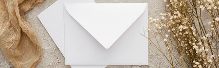 panoramic shot of white envelope near flowers and beige sackcloth on textured surface