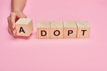 cropped view of woman holding wooden cube with A letter from adopt lettering on pink backgroundの写真素材