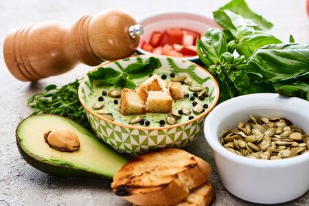bowl of delicious green vegetable creamy soup with croutons, black pepper and pumpkin seeds near...