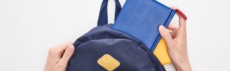 Panoramic shot of schoolgirl taking notepad from blue schoolbag isolated on white