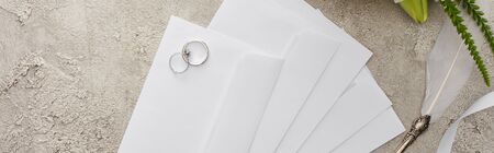panoramic shot of wedding rings on envelopes near quill pen on textured surface