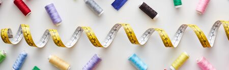 top view of measuring tape, colorful threads on white background