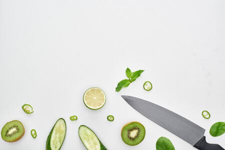 top view of knife, fresh cucumbers, kiwi, lime, peppers and greeneryの写真素材