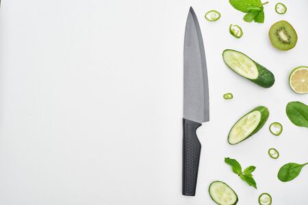top view of knife, fresh cucumbers, kiwi, lime, peppers and greenery