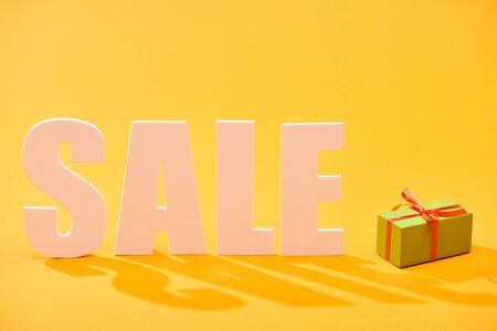 white sale lettering near wrapped gift box on bright orange backgroundの写真素材
