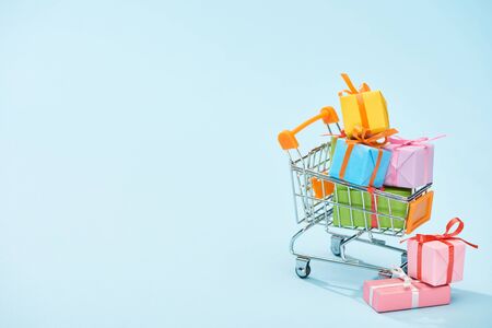 festive wrapped presents in shopping cart on blue background with copy space