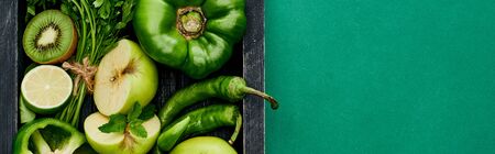 panoramic shot of apples, peppers, kiwi, greenery, lime in wooden box