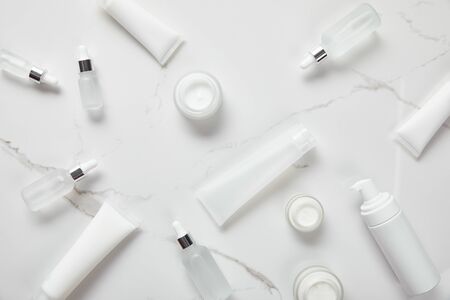top view of cosmetic glass bottles, jars with cream, moisturizer tubes, dispenser and jasmine on white surfaceの写真素材