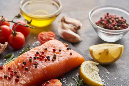 selective focus of raw salmon with seasoning, lemon and tomatoes on stone boardの写真素材