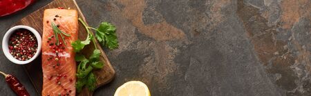 top view of salmon steak with peppercorns, parsley on wooden cutting board near lemon and chili...