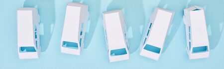 panoramic shot of miniature white trucks on blue background