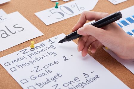 cropped view of woman holding black highlighter near cards on cork board