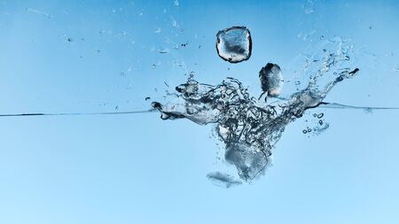transparent water with falling ice cubes and splash on blue backgroundの写真素材
