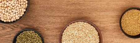 panoramic shot of bowls with chickpea, green beans and raw buckwheat on wooden surface