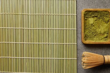 top view of green matcha powder on wooden board near bamboo whisk and table mat
